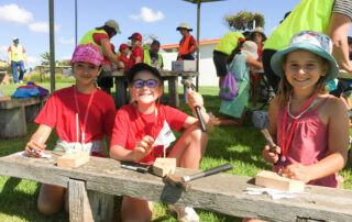 Kids sitting on a bench in the sun - proudly holding up their artwork